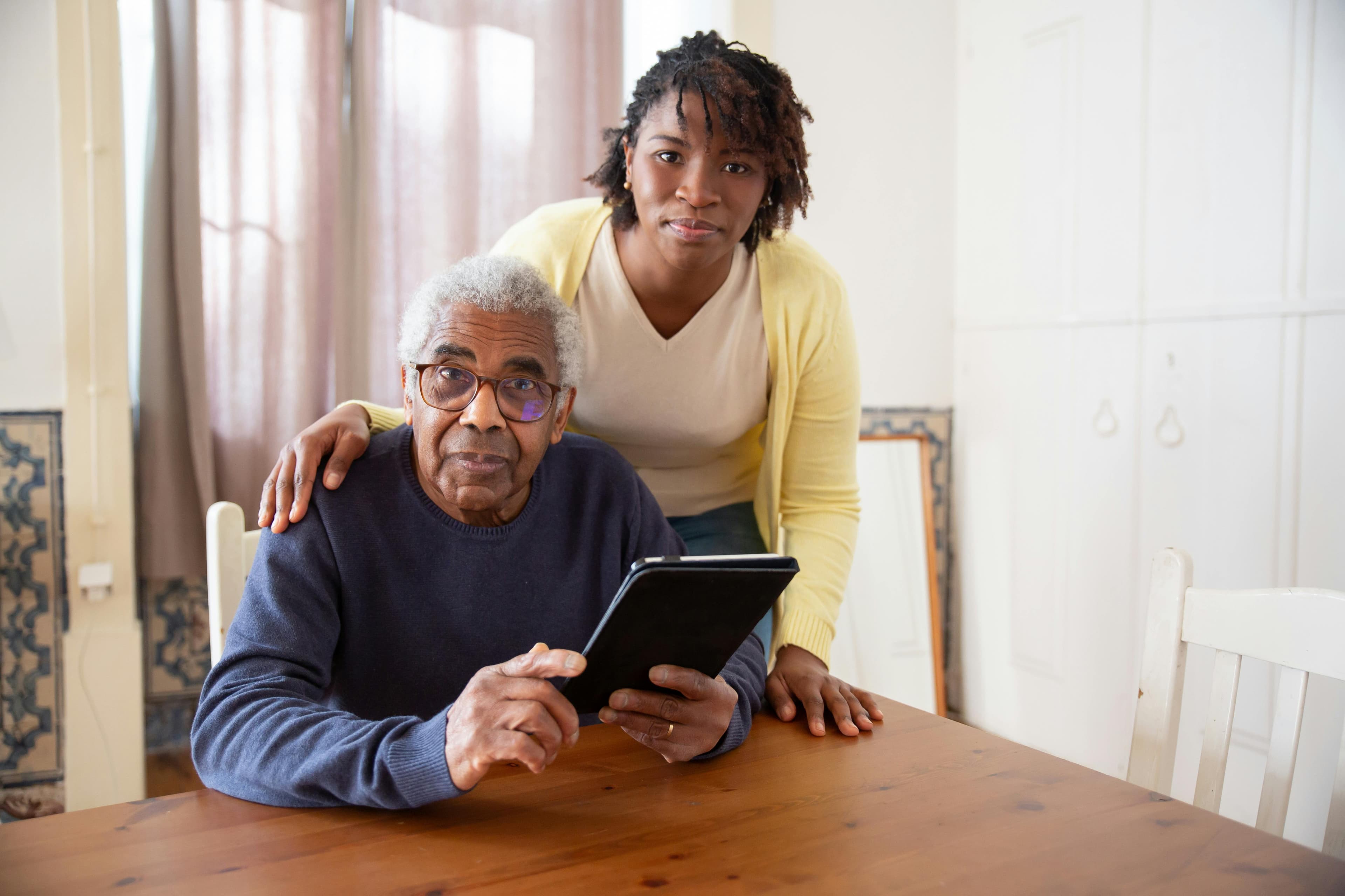 Happy elderly man with headphones using a tablet, sitting on couch at home